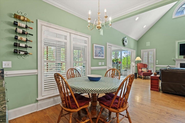 dining area featuring a chandelier, light wood-type flooring, ornamental molding, baseboards, and high vaulted ceiling