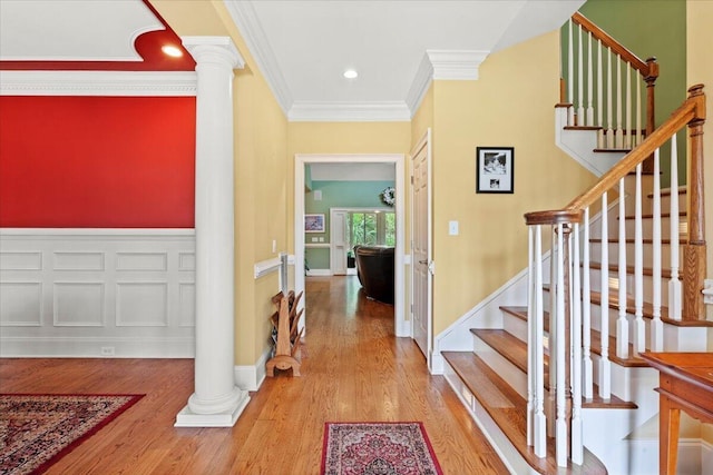 hallway featuring ornamental molding, wood finished floors, ornate columns, and stairs