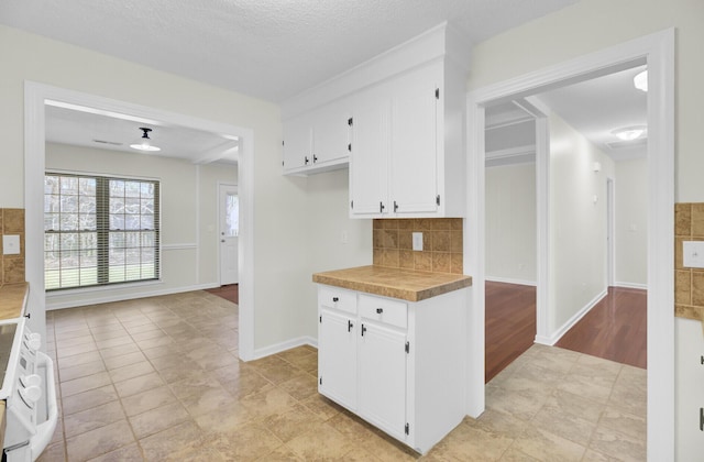 kitchen featuring baseboards, light countertops, white cabinets, a textured ceiling, and backsplash