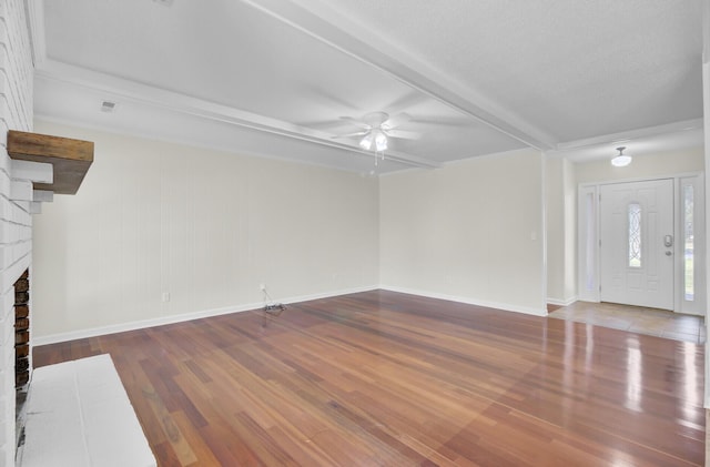 unfurnished living room featuring wood finished floors, baseboards, a ceiling fan, a fireplace, and beamed ceiling