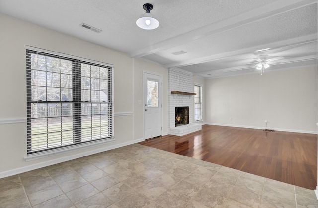 unfurnished living room with baseboards, visible vents, beam ceiling, and a brick fireplace