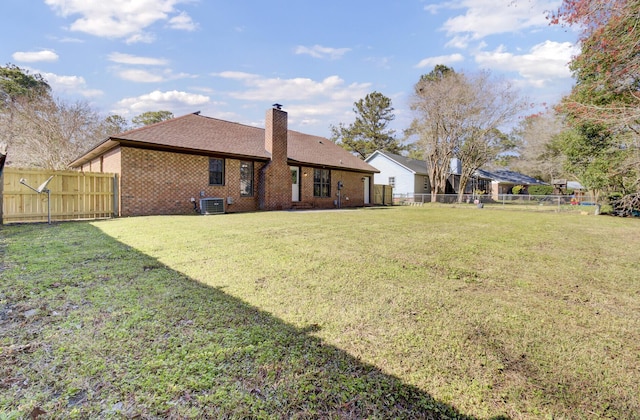 back of house featuring central AC unit, a yard, a fenced backyard, a chimney, and brick siding