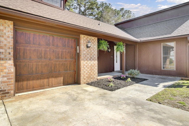 doorway to property with concrete driveway, brick siding, and a shingled roof