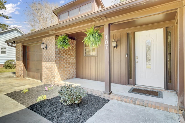 doorway to property featuring brick siding, covered porch, and an attached garage