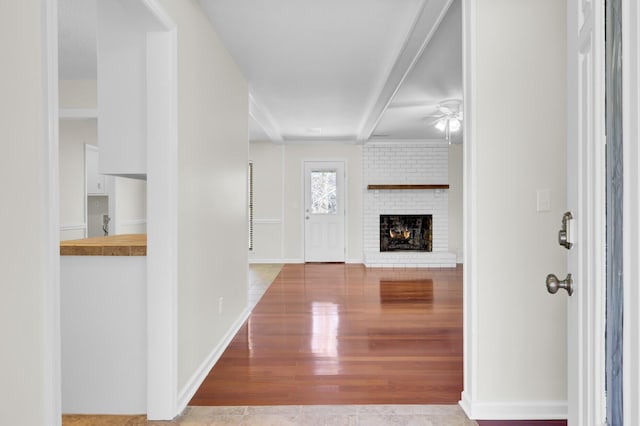 foyer with a brick fireplace, baseboards, ceiling fan, and wood finished floors