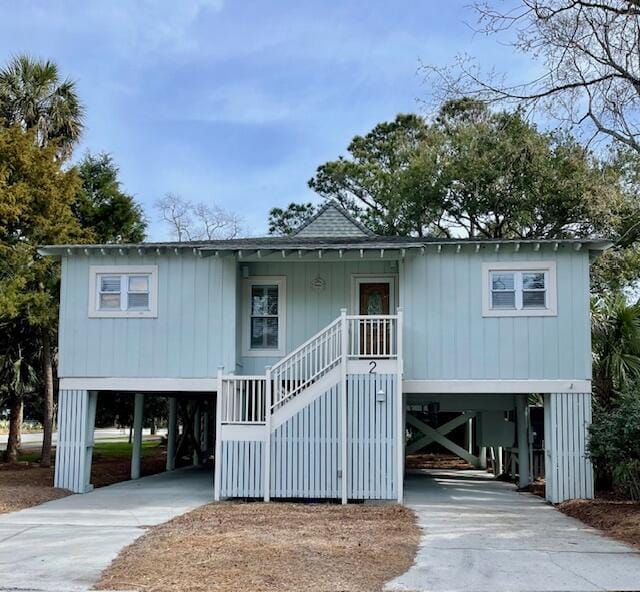 coastal home with roof with shingles, stairway, a carport, and concrete driveway