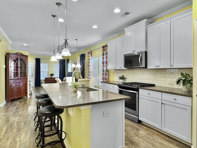 kitchen featuring hanging light fixtures, stainless steel appliances, tasteful backsplash, white cabinets, and a center island with sink