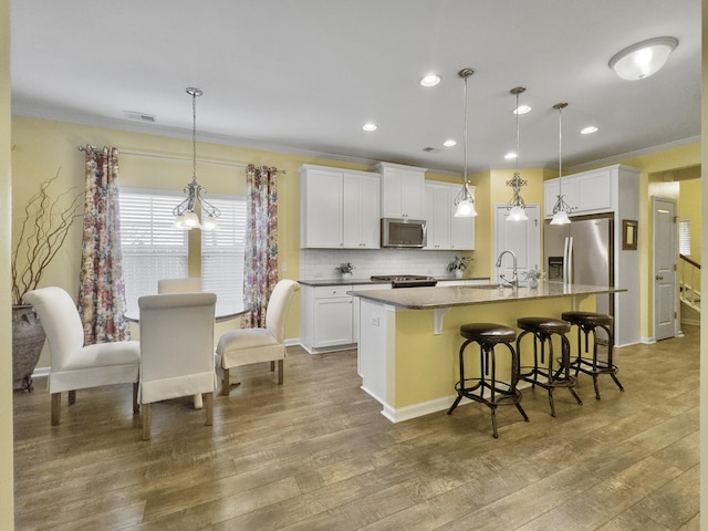 kitchen with pendant lighting, an island with sink, sink, white cabinets, and stainless steel appliances