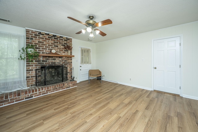 unfurnished living room with a textured ceiling, light hardwood / wood-style flooring, ceiling fan, and a brick fireplace