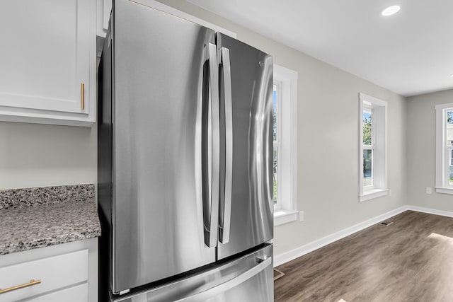 kitchen featuring stainless steel refrigerator, white cabinetry, dark hardwood / wood-style flooring, and light stone countertops