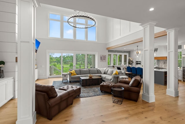 living room with a high ceiling, ornate columns, light hardwood / wood-style floors, and a notable chandelier