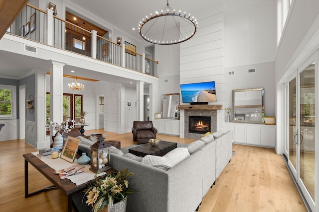 living room featuring an inviting chandelier, decorative columns, a high ceiling, and light hardwood / wood-style flooring