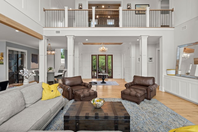 living room with light hardwood / wood-style floors, an inviting chandelier, and ornate columns