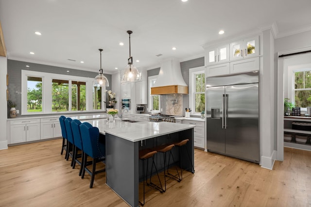 kitchen featuring stove, premium range hood, white cabinets, a breakfast bar, and built in fridge