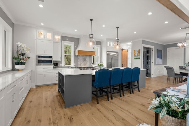 kitchen with white cabinets, a kitchen island, custom range hood, light hardwood / wood-style floors, and appliances with stainless steel finishes