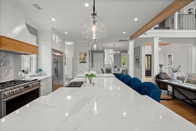 kitchen featuring light stone counters, pendant lighting, custom range hood, stainless steel appliances, and ornamental molding