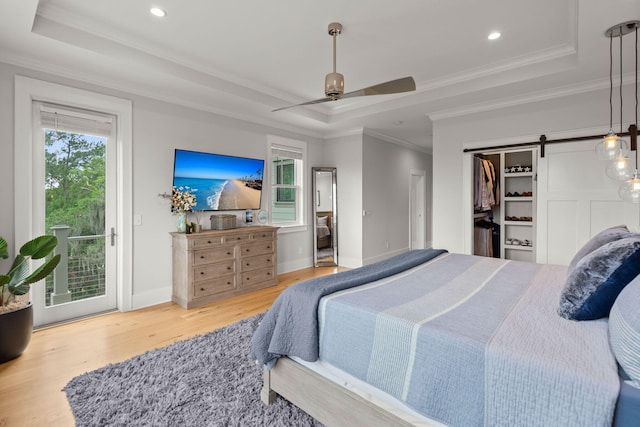 bedroom with ceiling fan, a tray ceiling, light hardwood / wood-style flooring, and a barn door