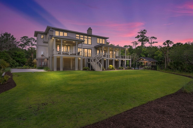 back house at dusk with a lawn, a sunroom, and a garage