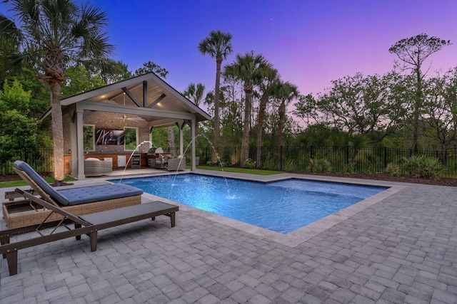 pool at dusk featuring a patio, a gazebo, ceiling fan, pool water feature, and an outdoor living space