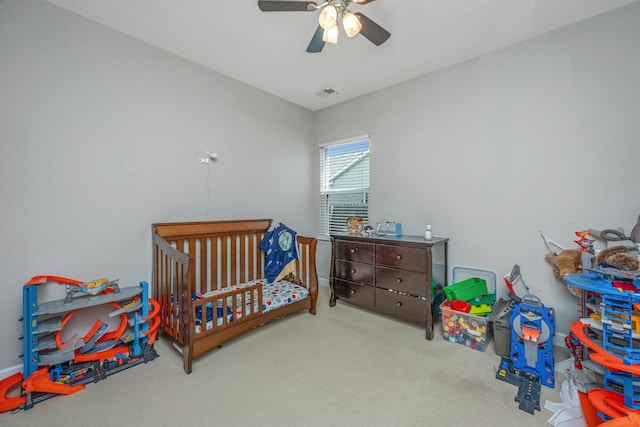 carpeted bedroom featuring ceiling fan and a nursery area