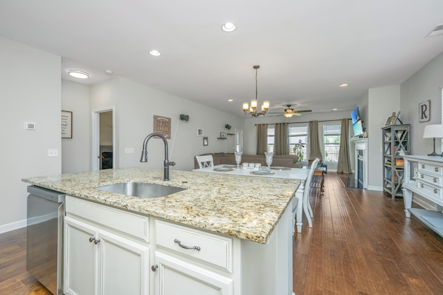 kitchen with sink, dark wood-type flooring, an island with sink, and light stone counters