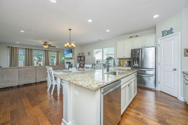 kitchen with sink, a center island with sink, white cabinetry, stainless steel appliances, and ceiling fan with notable chandelier