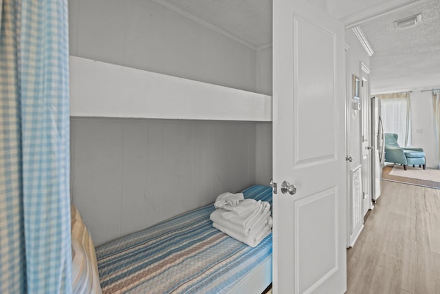 bedroom with visible vents, freestanding refrigerator, ornamental molding, wood finished floors, and a textured ceiling