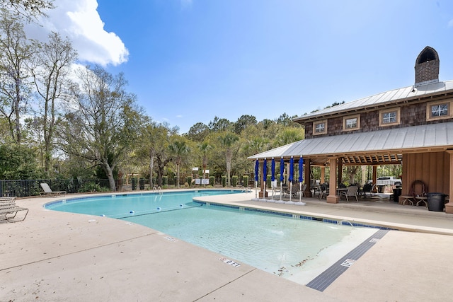 community pool with a patio, fence, and view of wooded area