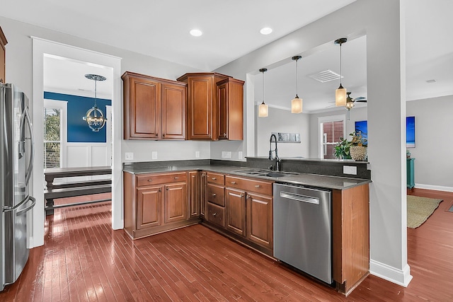 kitchen featuring appliances with stainless steel finishes, a sink, dark countertops, brown cabinetry, and recessed lighting