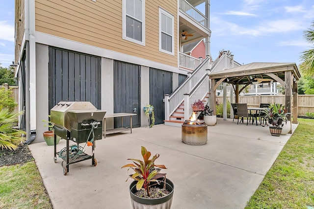 view of patio featuring an outdoor fire pit, a gazebo, fence, a ceiling fan, and stairs