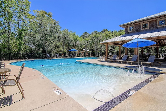 community pool featuring fence, a patio area, and view of wooded area