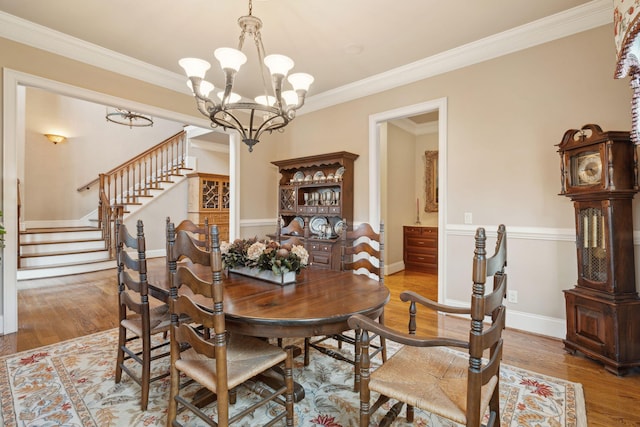 dining space with light wood-style flooring, ornamental molding, a chandelier, baseboards, and stairs