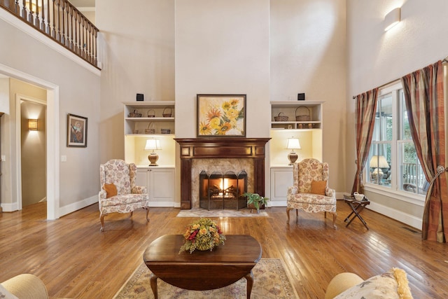 sitting room with baseboards, a high end fireplace, a towering ceiling, and light wood-style floors