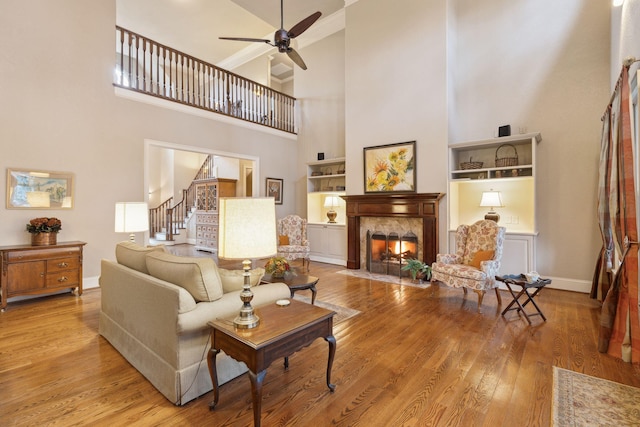 living room with light wood finished floors, baseboards, ceiling fan, stairway, and a high end fireplace