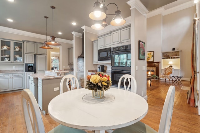 dining space with a lit fireplace, crown molding, light wood-style floors, a notable chandelier, and recessed lighting