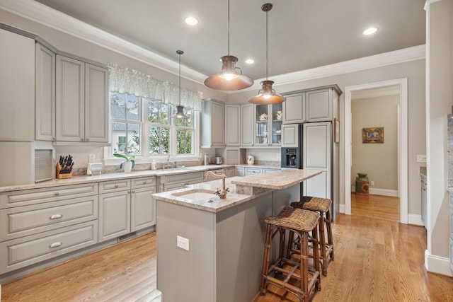 kitchen with light stone counters, gray cabinets, glass insert cabinets, a kitchen island with sink, and a sink