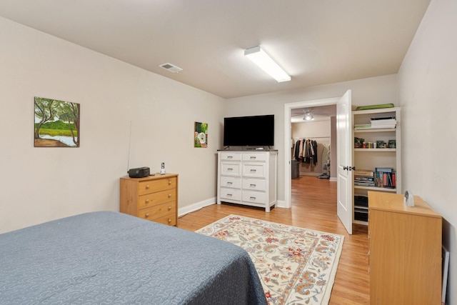 bedroom with a spacious closet, wood finished floors, visible vents, and baseboards