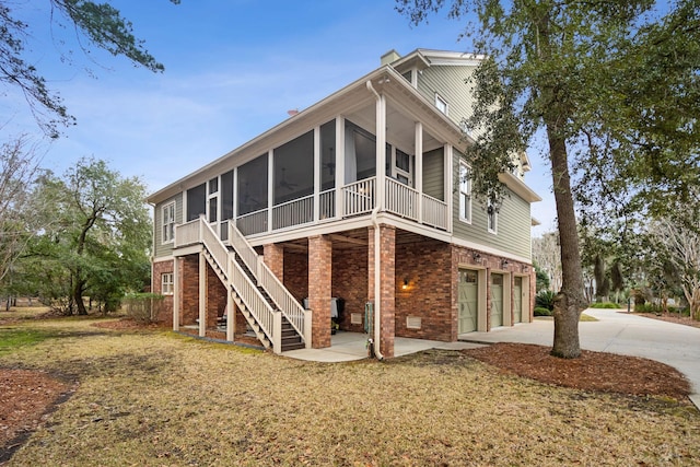 exterior space featuring brick siding, a sunroom, a garage, driveway, and stairs