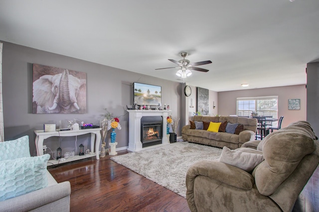 living room featuring baseboards, a ceiling fan, a glass covered fireplace, and wood finished floors