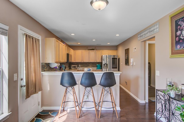 kitchen featuring tasteful backsplash, light brown cabinets, stainless steel fridge, a peninsula, and light countertops