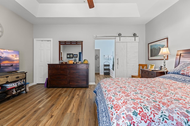 bedroom featuring hardwood / wood-style floors, a raised ceiling, ceiling fan, and a barn door