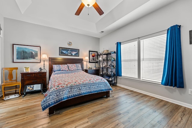 bedroom featuring a raised ceiling, ceiling fan, and light hardwood / wood-style flooring