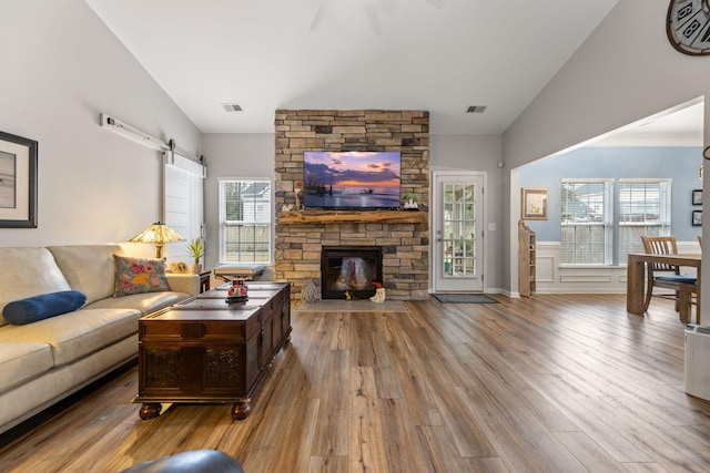 living room with lofted ceiling, a stone fireplace, wood-type flooring, and a barn door