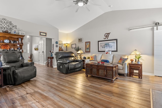 living room with vaulted ceiling, a barn door, ceiling fan, and light wood-type flooring