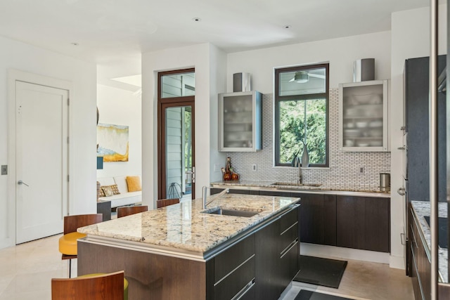 kitchen with decorative backsplash, a kitchen island, light stone countertops, and sink