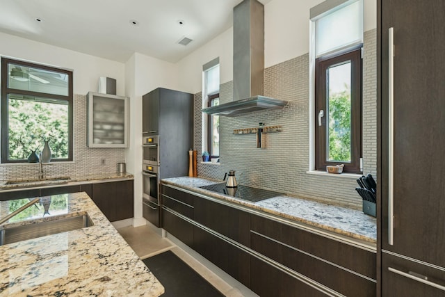 kitchen with stainless steel oven, wall chimney range hood, decorative backsplash, light stone countertops, and black electric cooktop