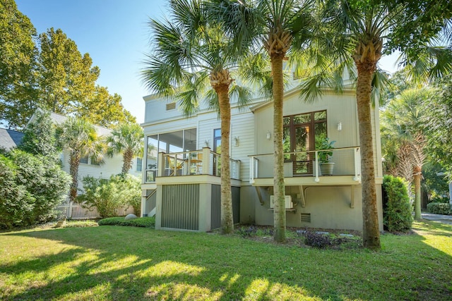 rear view of house with a sunroom, a balcony, a wall mounted AC, and a lawn