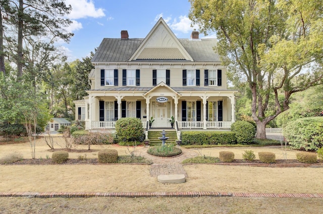 view of front of home with a porch, a chimney, and metal roof