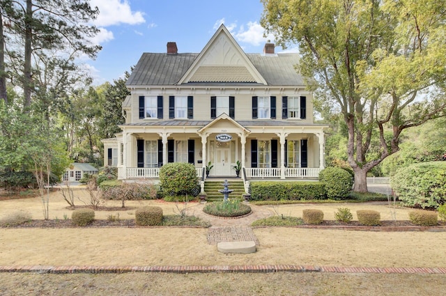 view of front of house with covered porch, a chimney, and metal roof