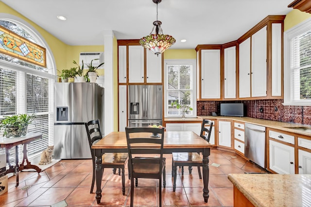 kitchen with appliances with stainless steel finishes, light tile patterned flooring, decorative light fixtures, and tasteful backsplash